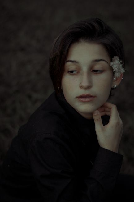 A thoughtful woman with short hair and a flower accessory, gazing pensively.