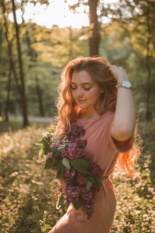 Woman Carrying Flowers While Walking Near Trees during Golden Hour