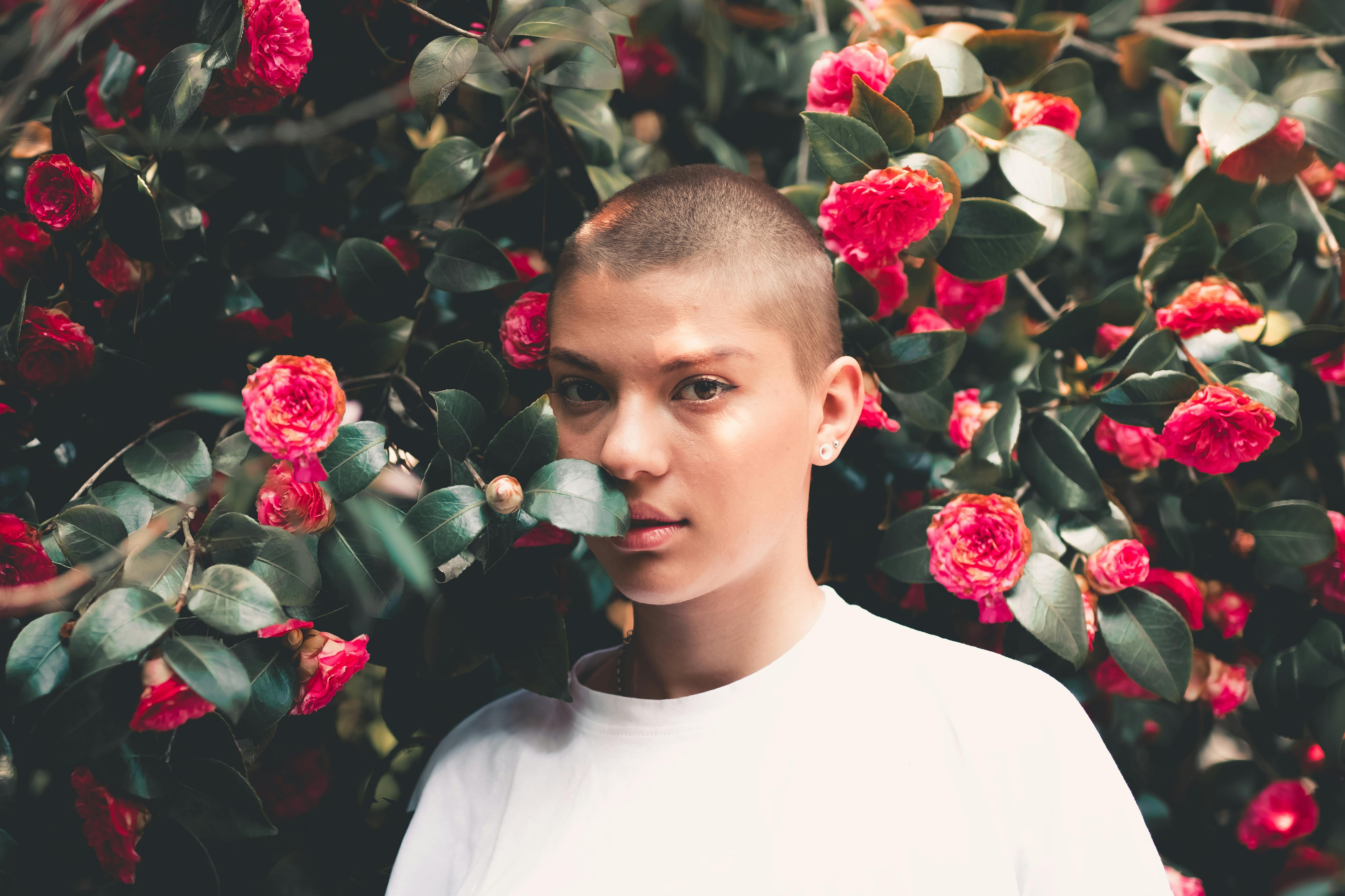 A striking portrait of a woman in a white t-shirt surrounded by vivid red flowers.