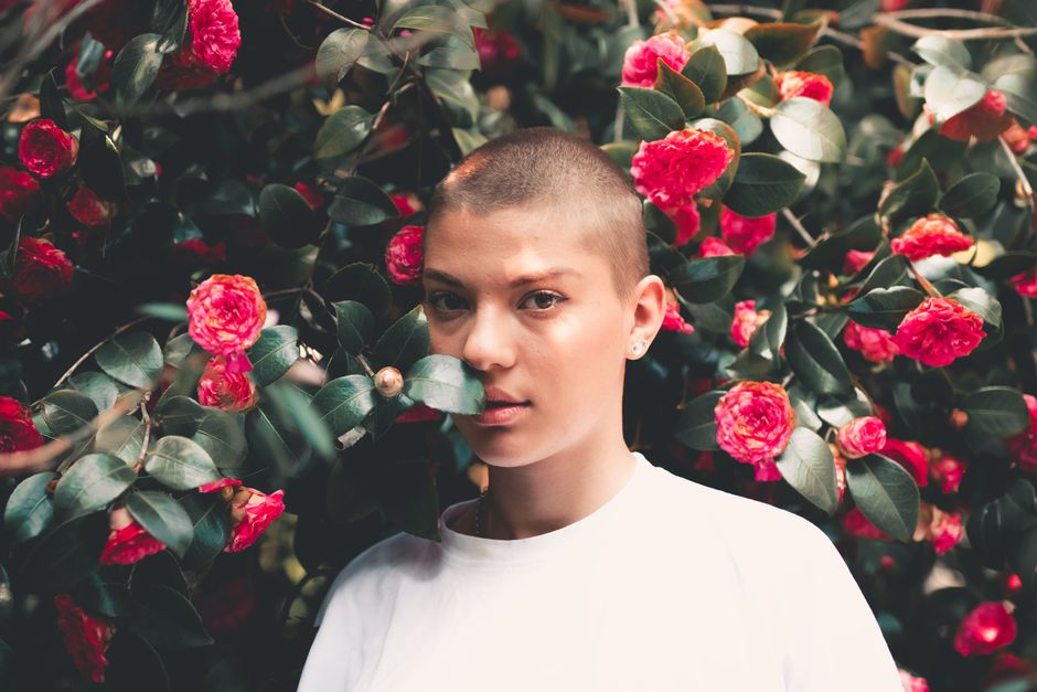 A striking portrait of a woman in a white t-shirt surrounded by vivid red flowers.