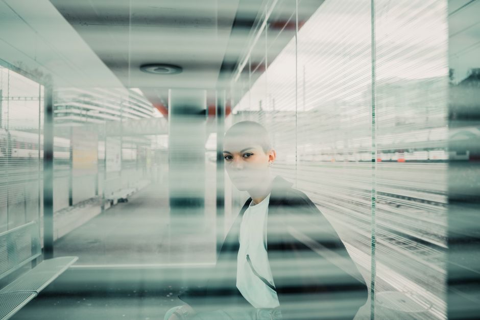 Bald person in a modern, urban environment with reflections.