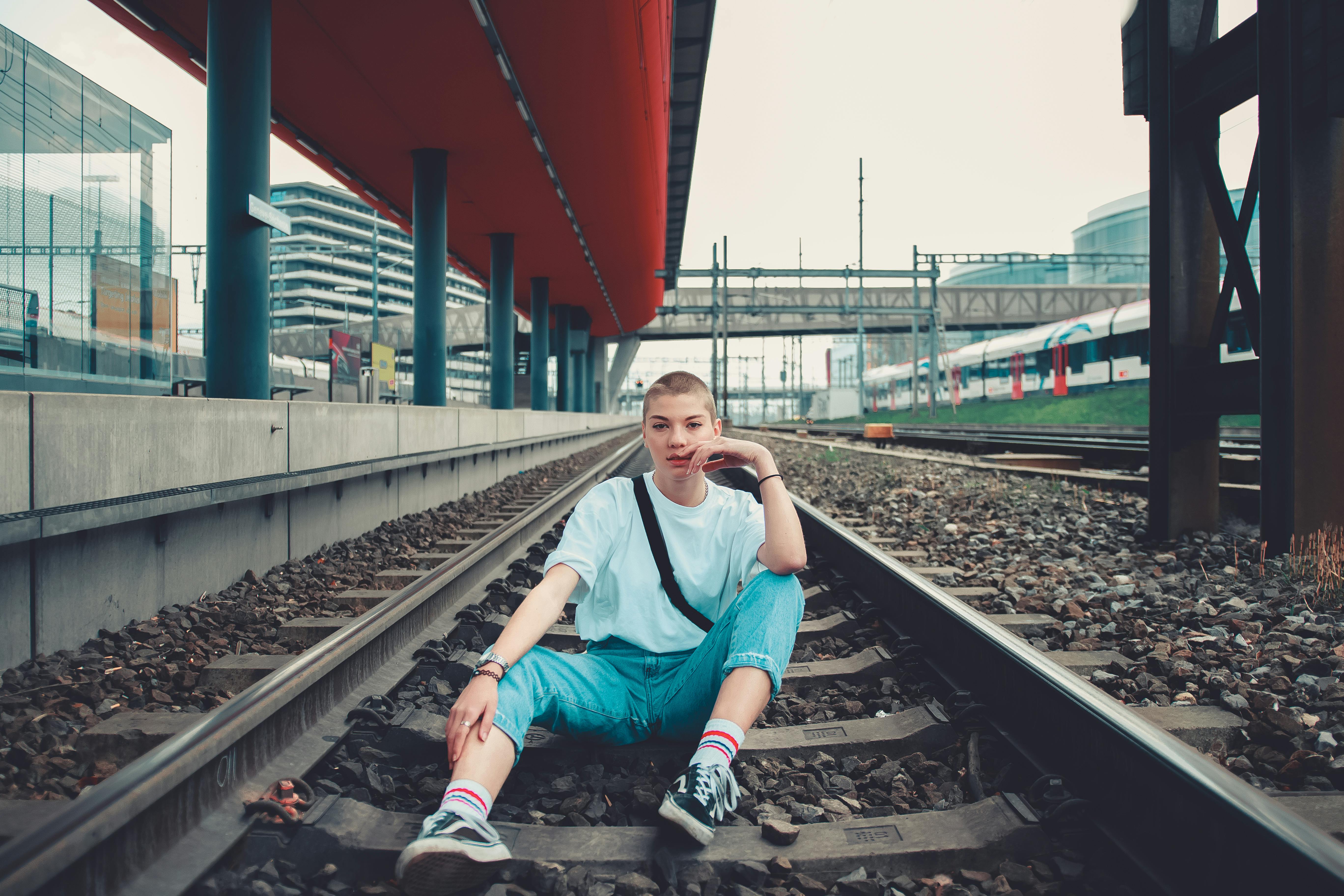 一位年轻女子身着休闲装，充满现代气息地坐在城市铁轨上
