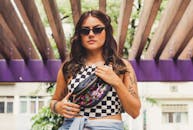 一位纹身时尚的年轻女子戴着太阳镜，拿着一个五颜六色的流浪包，在户外摆姿势