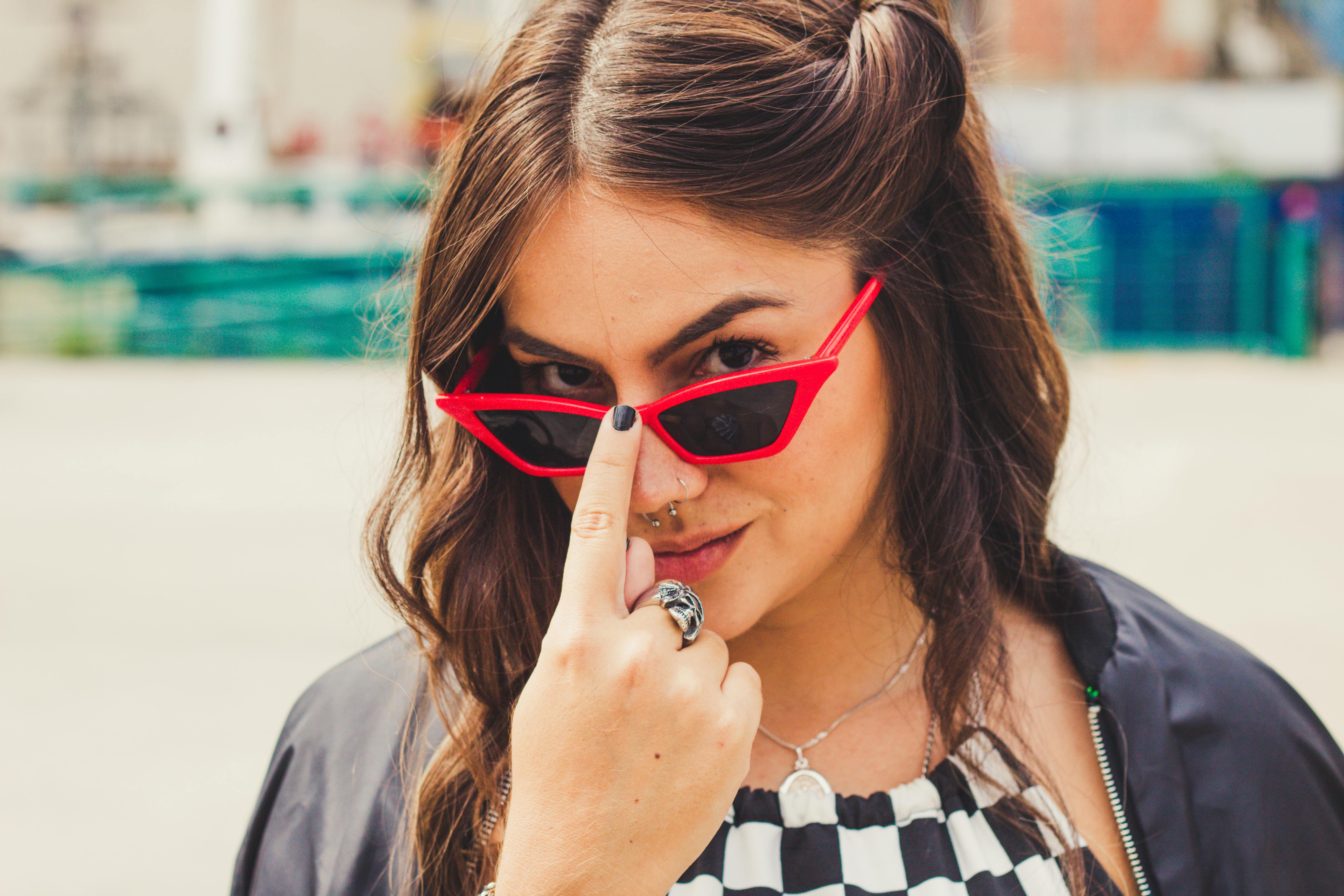 一位戴着红色太阳镜的自信女性在户外摆出俏皮的姿势