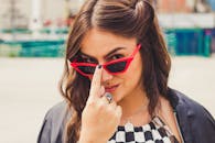 一位戴着红色太阳镜的自信女性在户外摆出俏皮的姿势