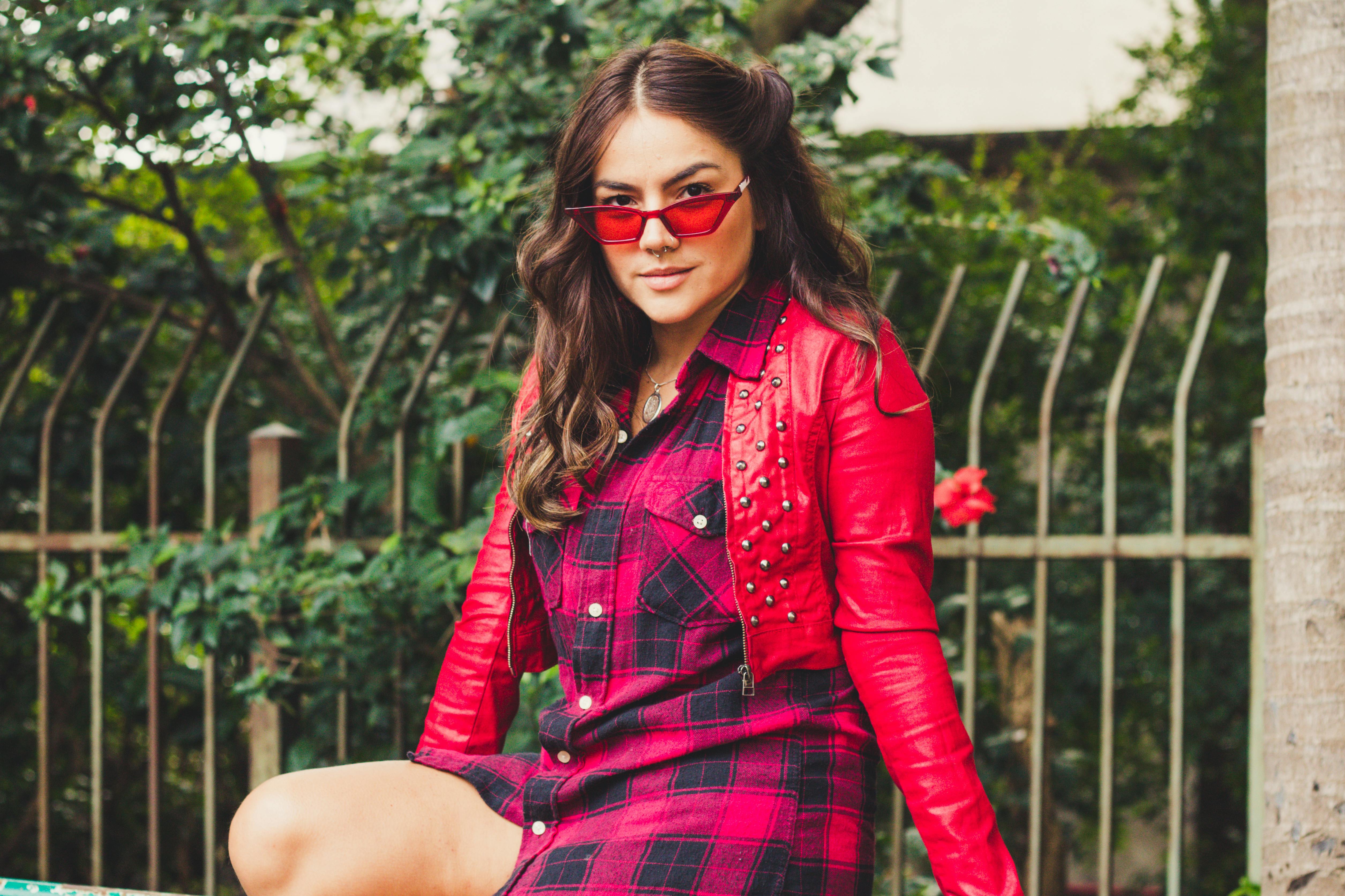 一位穿着时髦的女人在户外穿着红色格子衬衫和夹克摆姿势