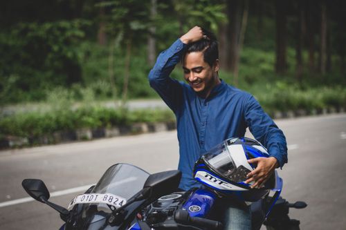 Free A young man holding a helmet standing next to a motorcycle on a scenic road. Stock Photo