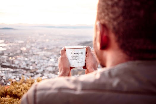 一名男子一边用露营杯喝着热饮，一边欣赏风景，尽显悠闲与放松