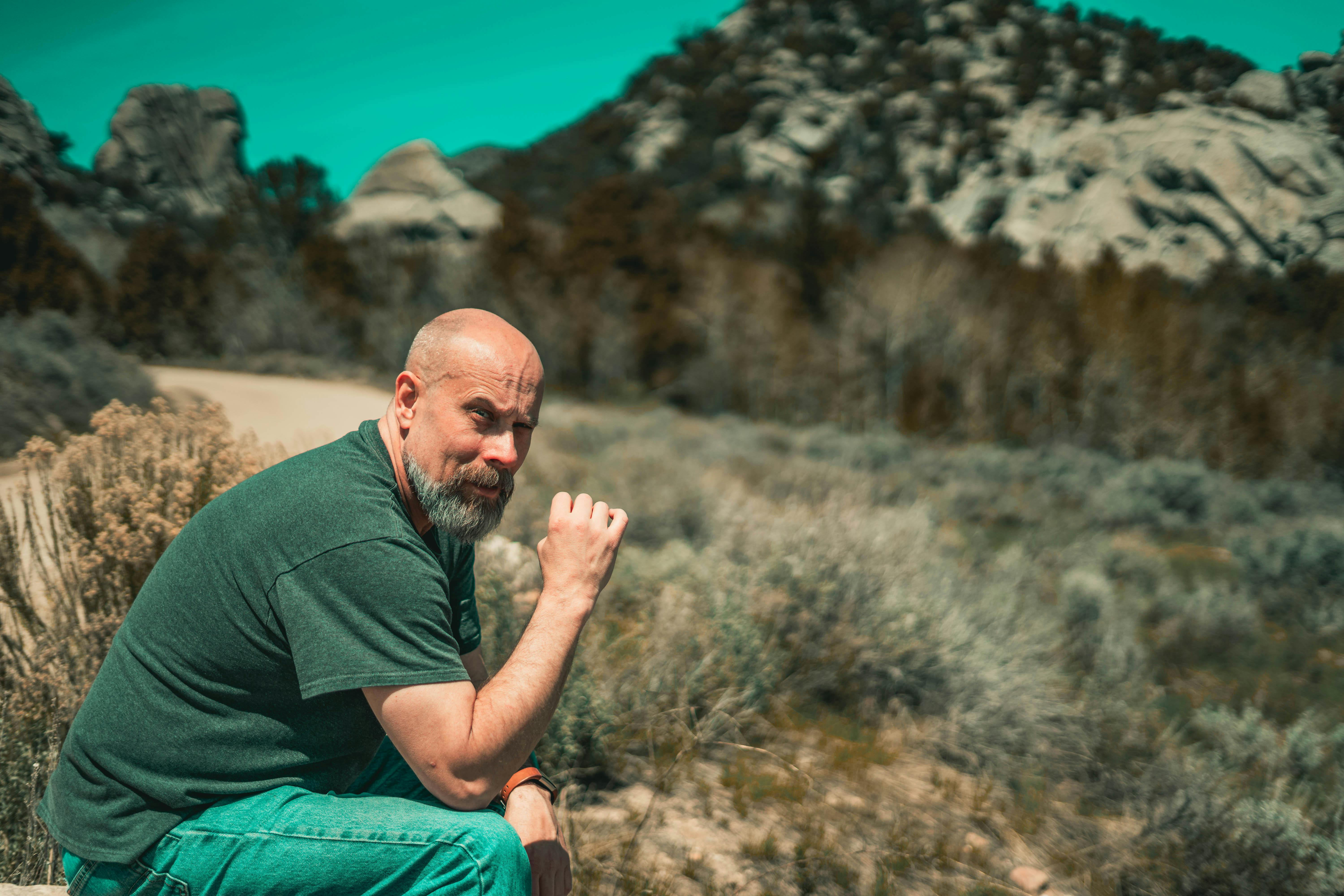 一位留着胡须的秃头男子坐在风景如画的户外，在岩石山丘的环绕中放松身心