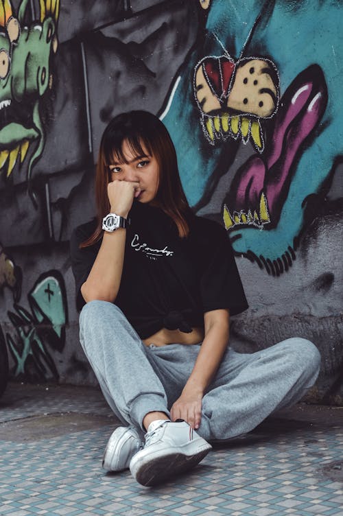 Free Photo of Woman in Black Crew-neck T-shirt and Gray Track Pants Sitting Beside Graffiti Wall Stock Photo