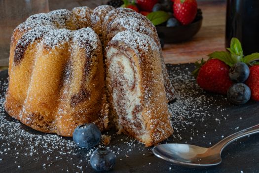 A close-up of a marble bundt cake with powdered sugar and fresh berries, perfect for dessert.