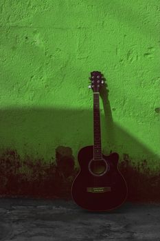 A lone acoustic guitar leaning against a vivid green wall, casting a long shadow.