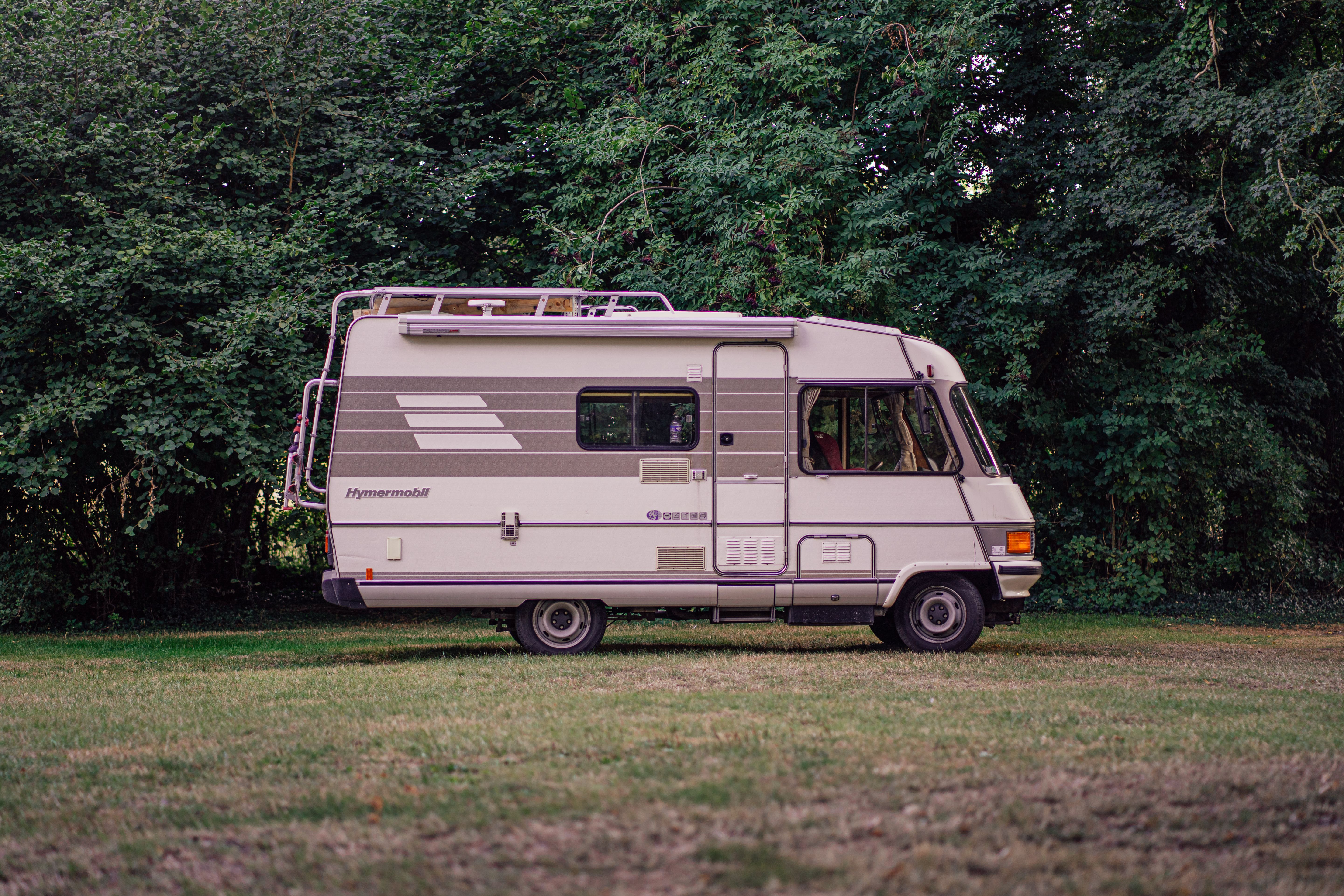 A classic Hymermobil RV parked amidst green trees and grass, perfect for exploring the outdoors.