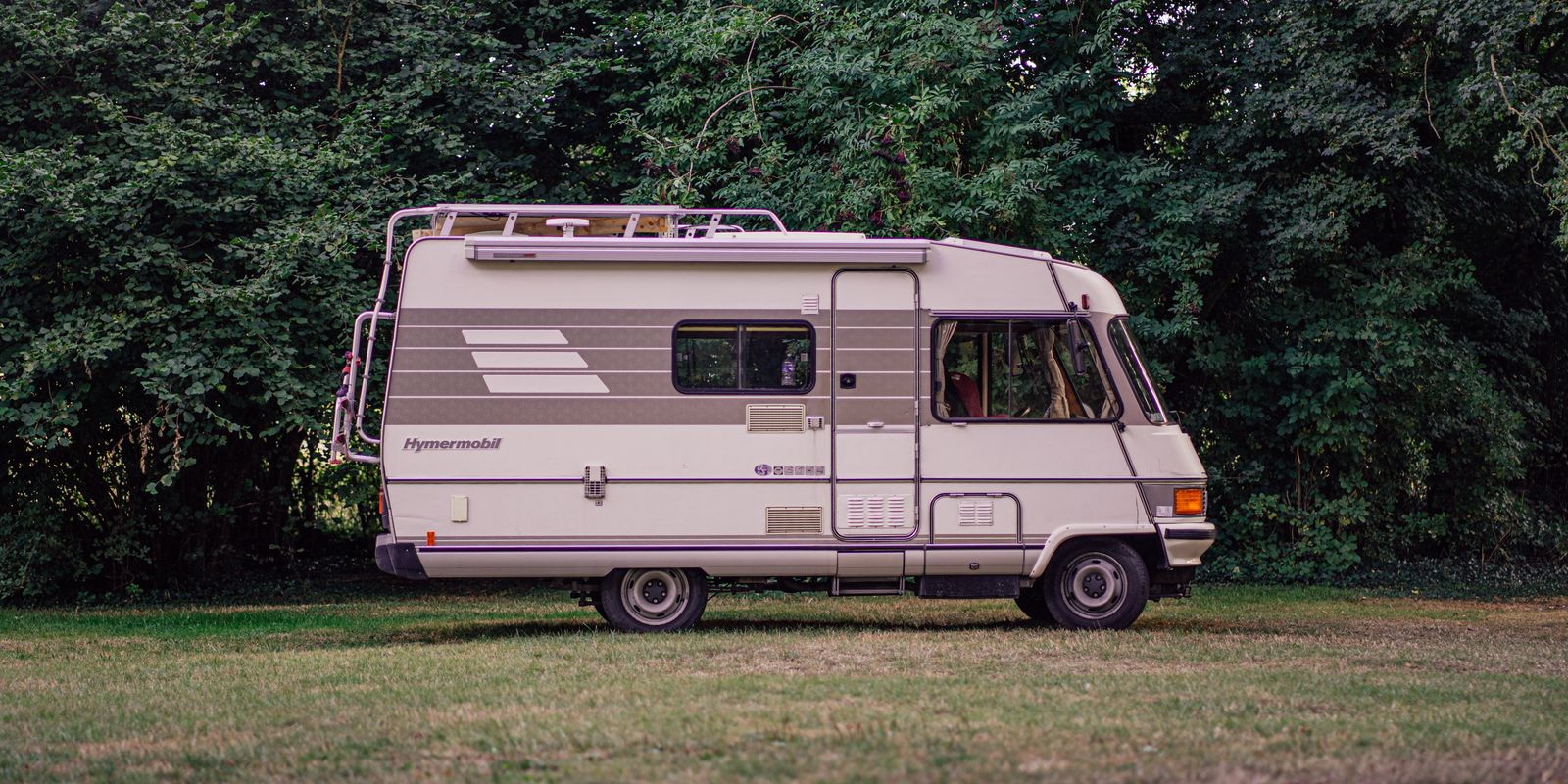 A classic RV parked among green trees and grass