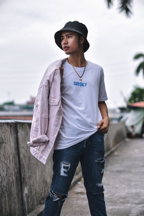 Free Fashionable young man poses in trendy streetwear with hat and ripped jeans in an urban environment. Stock Photo