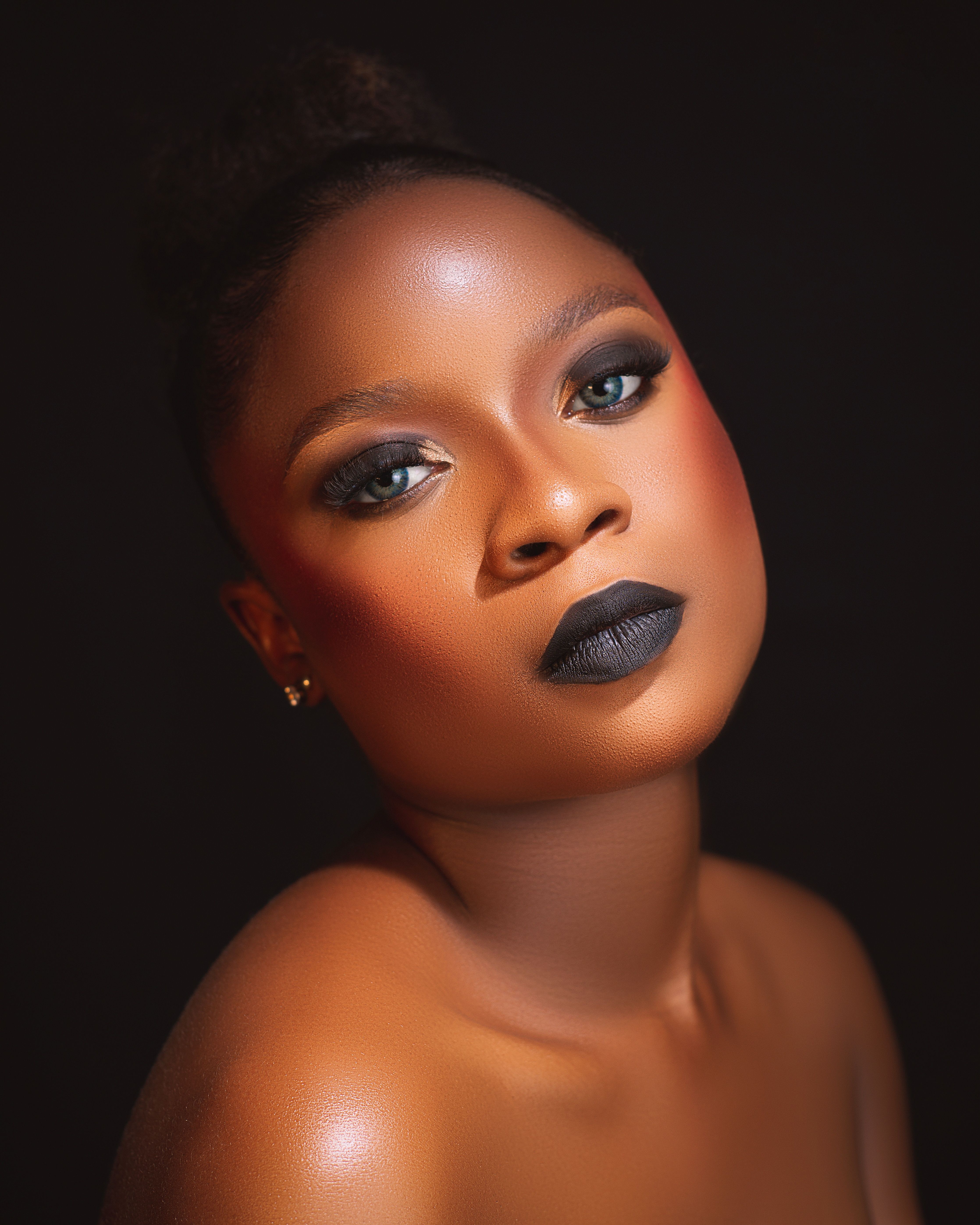 Stunning portrait of a woman featuring bold makeup and poised expression against a dark background.
