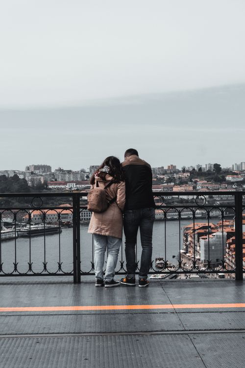 Free Couple standing on Dom Luís I Bridge in Porto, overlooking the Douro River and cityscape. Stock Photo