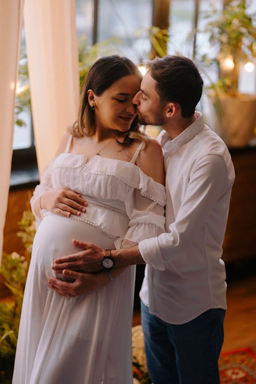 Free A pregnant woman and her husband are kissing in a room Stock Photo
