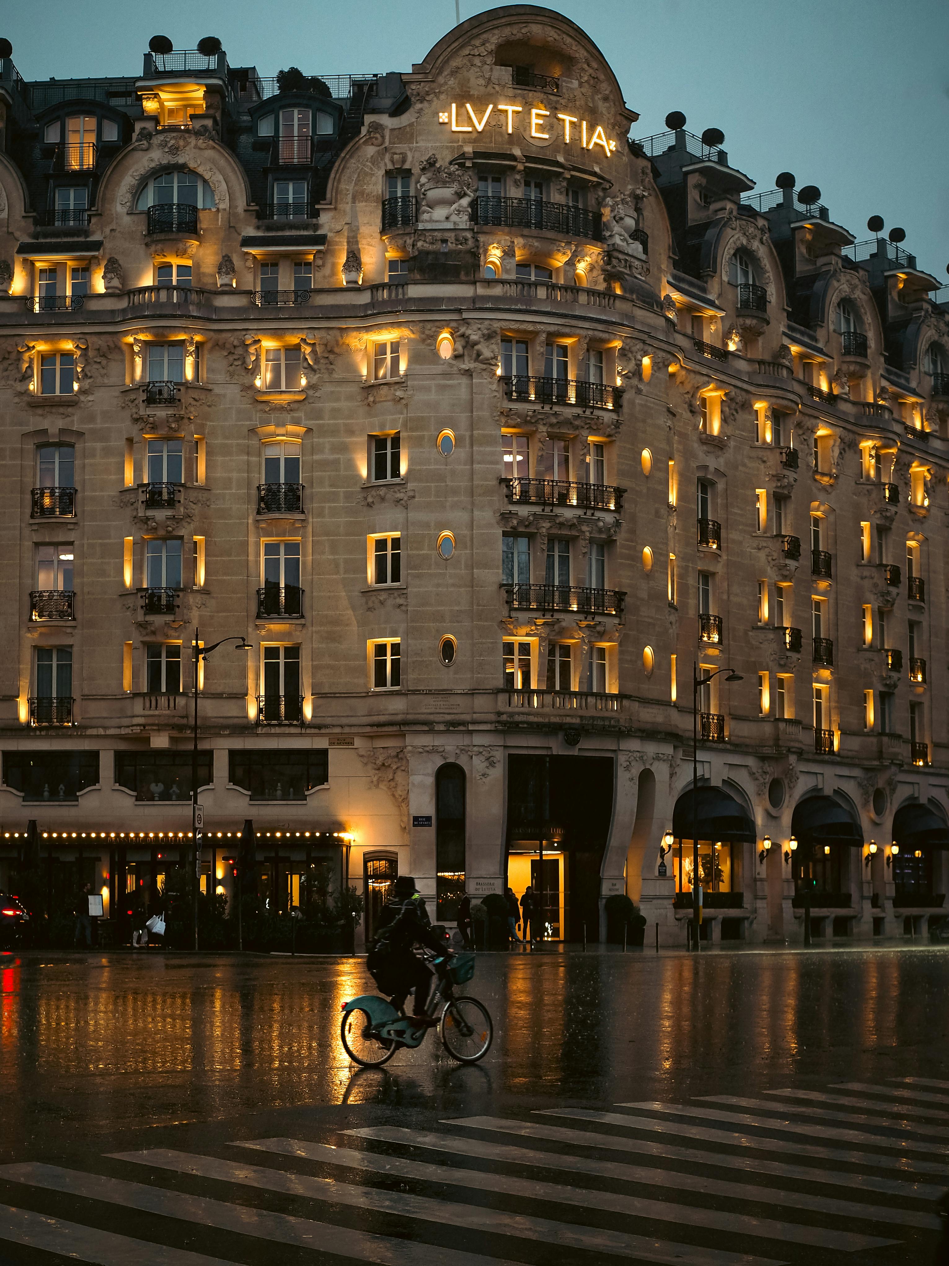 Captivating view of the Lit-up Lutetia Hotel in Paris during twilight with a cyclist on the street.