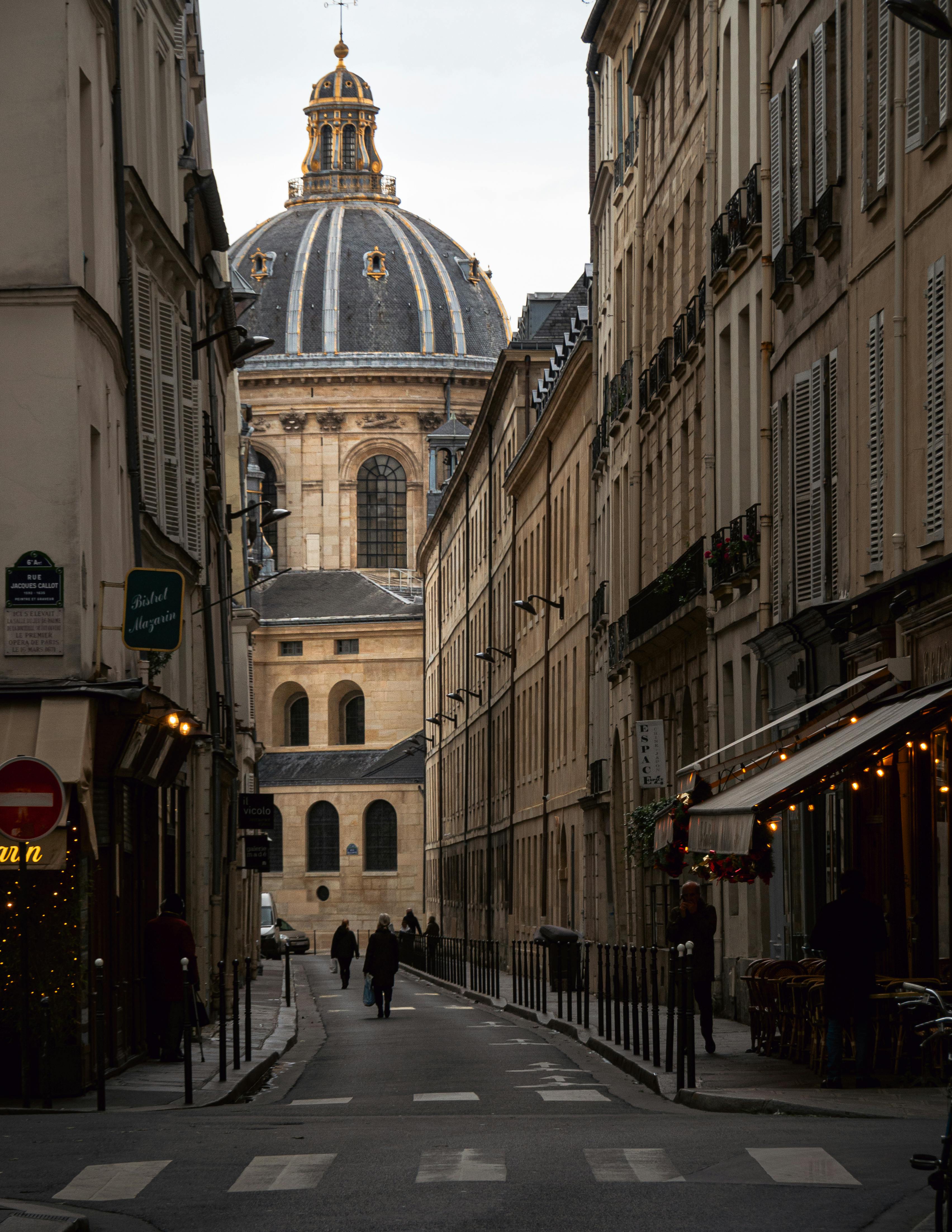 A picturesque view of a Paris street with the iconic dome of Institut de France in the background.
