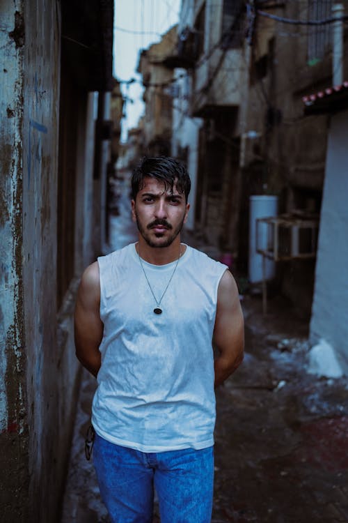 A man standing in an alleyway with a white tank top