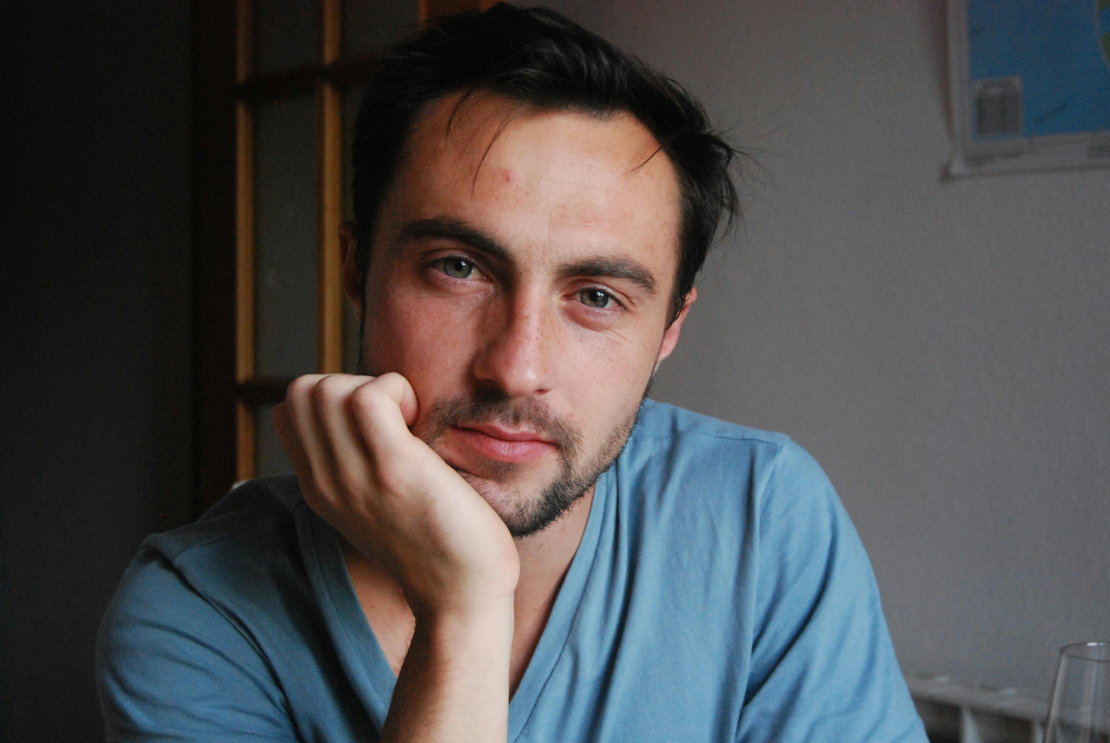 A thoughtful man in a blue shirt indoors, gazing at the camera under natural light.