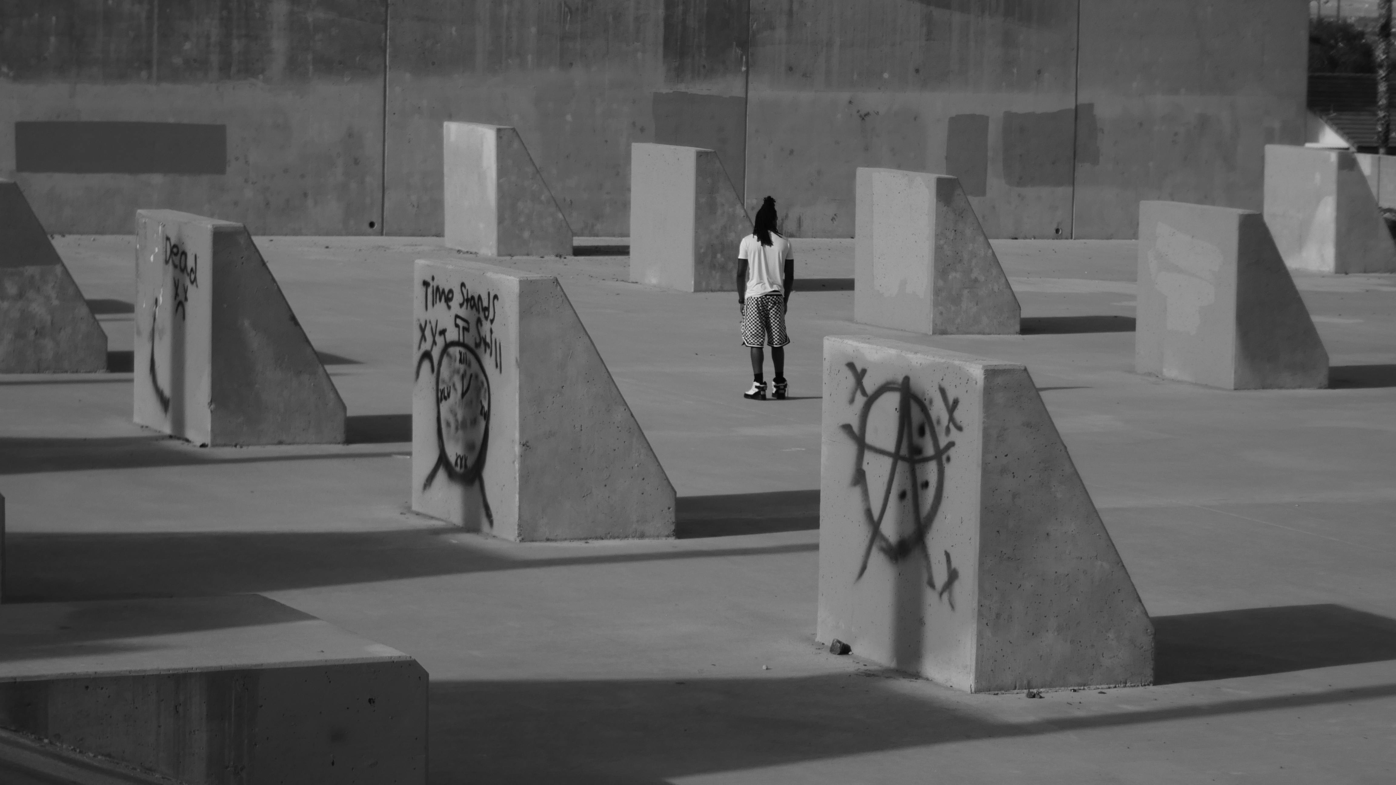 一张黑白图像中，一名男子站在涂鸦覆盖的混凝土结构里
