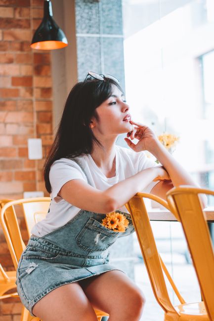 Woman in casual denim attire relaxed in a cozy café with yellow chairs and warm lighting.