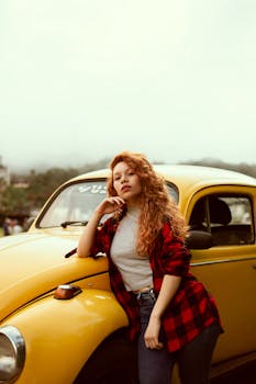 Portrait of a woman in casual fashion standing confidently by a yellow Volkswagen Beetle outdoors.