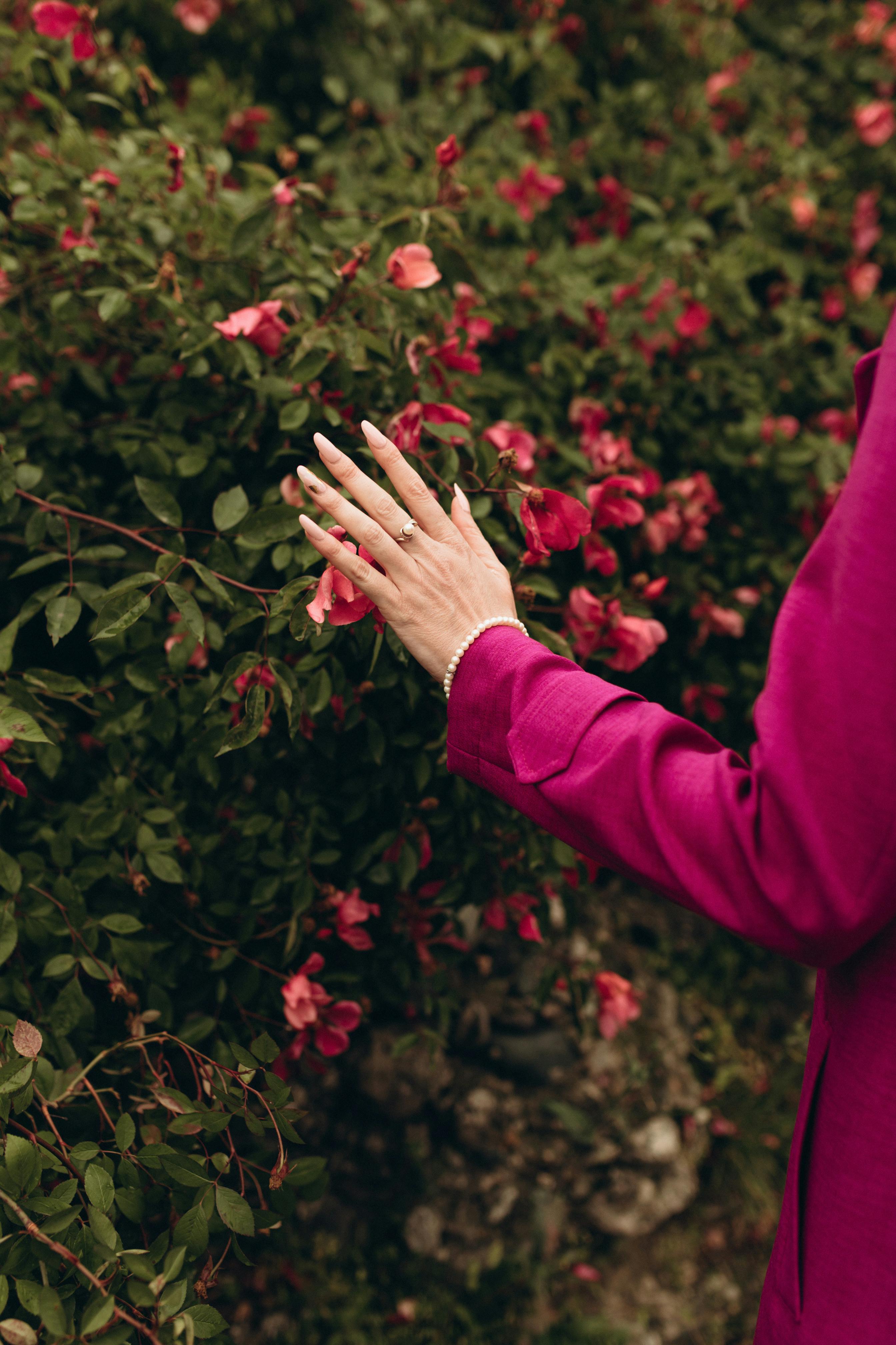A woman's hand gently touches blooming pink roses, showcasing nature and style harmony.