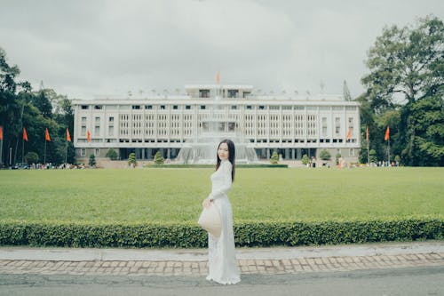 A woman in a white dress stands in front of a large building