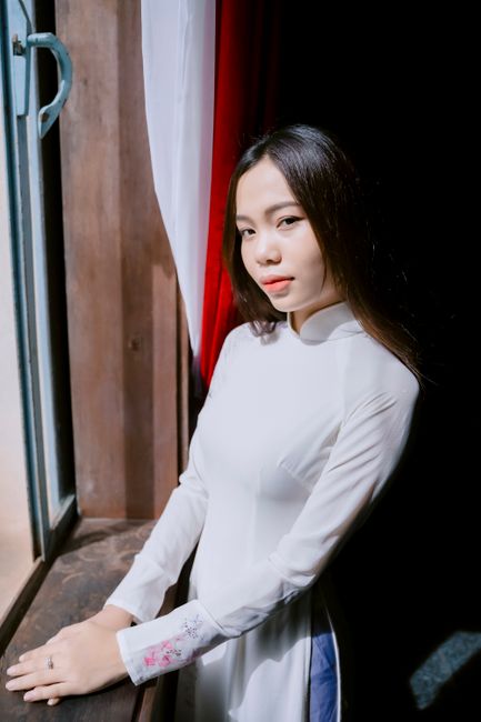 Elegant young Vietnamese woman in ao dai, posing by a sunlit window, showcasing traditional beauty and culture.