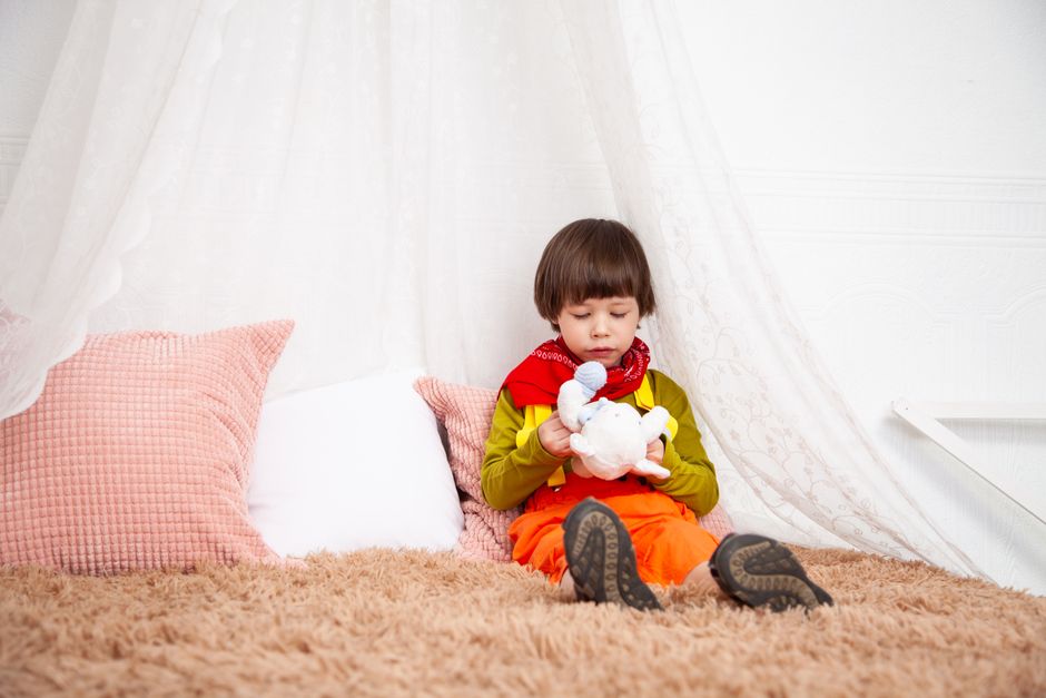 Adorable child sitting indoors with a toy, showcasing innocence and playfulness.
