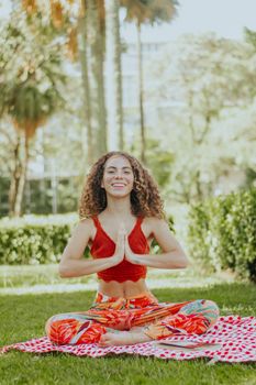 Smiling woman meditating on a mat in a sunny park, exuding calm and relaxation.