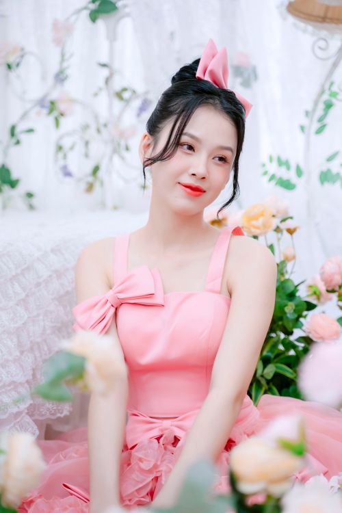 Free Portrait of an elegant woman in a pink dress sitting amidst floral decorations. Stock Photo