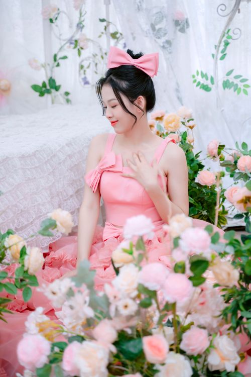 Free A woman in a pink gown sits gracefully among pink and white flowers, embodying elegance. Stock Photo