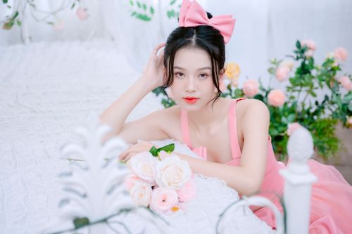 Free Asian woman in elegant pink dress posing with roses in a floral-themed bedroom. Stock Photo