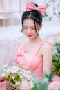 一位身穿粉色连衣裙的年轻女子优雅地坐在室内，手里摆着一篮子雏菊，散发着优雅的气息