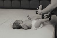 A mother lovingly dresses her newborn baby lying on a bed in an intimate black and white setting.