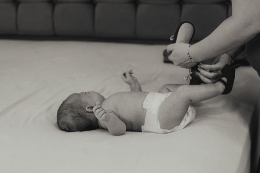 A mother lovingly dresses her newborn baby lying on a bed in an intimate black and white setting.