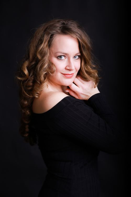 Free Studio portrait of a smiling woman with curly hair in an elegant black top posing against a dark background. Stock Photo