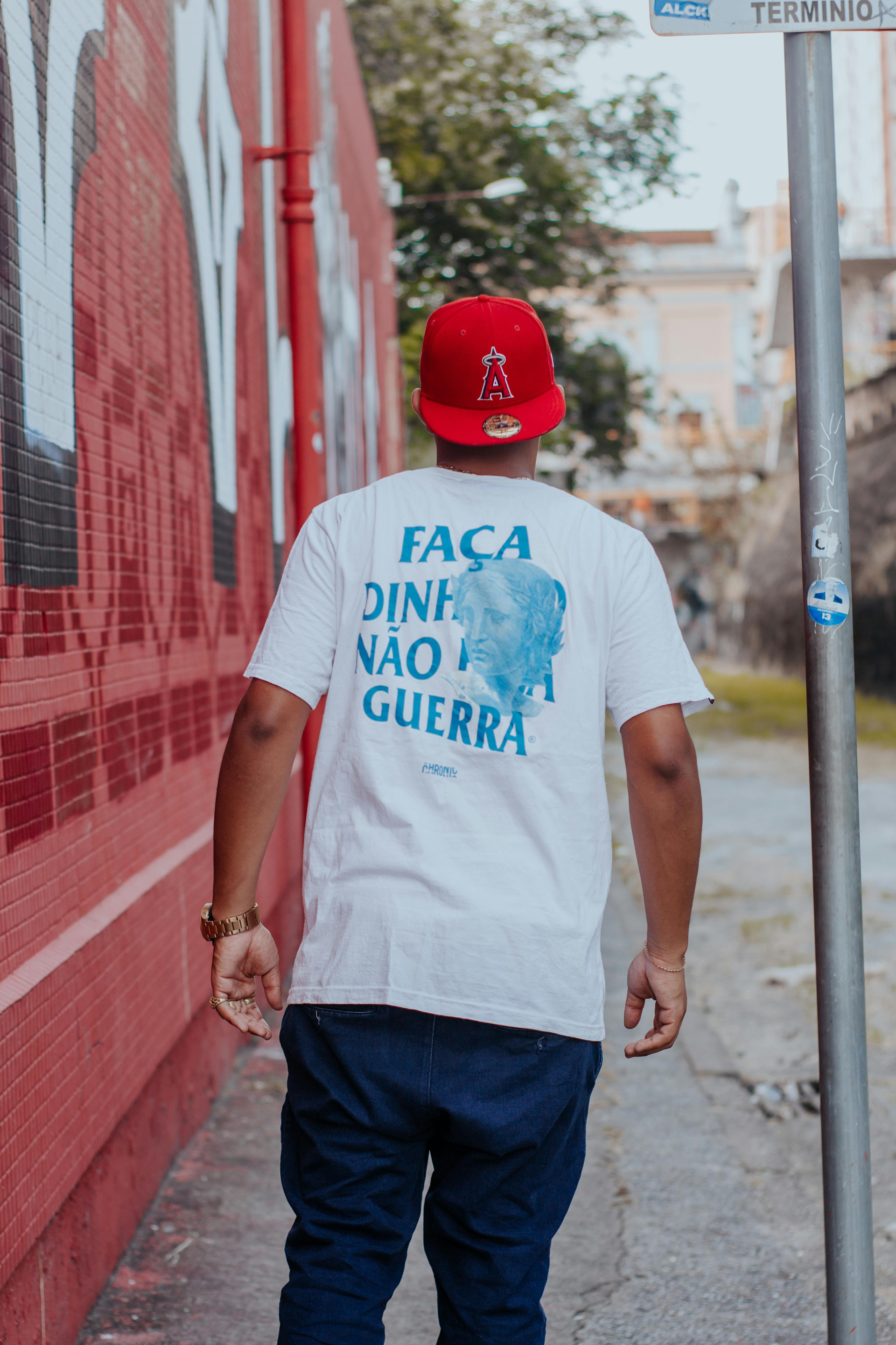 Back view of a man in white t-shirt and red cap walking in a city street.