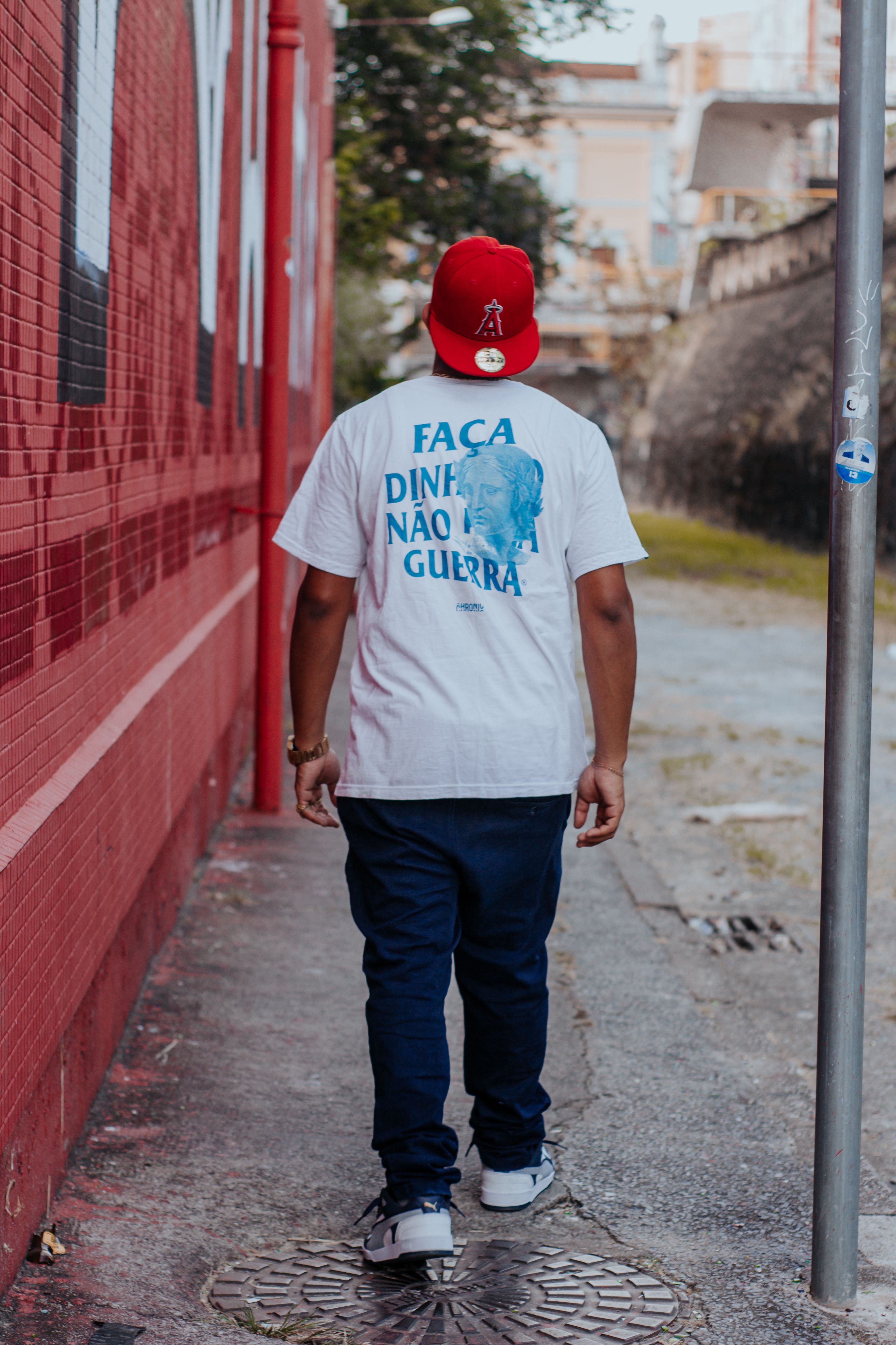 Back view of man in urban setting wearing a red cap and jeans, walking down a sidewalk.