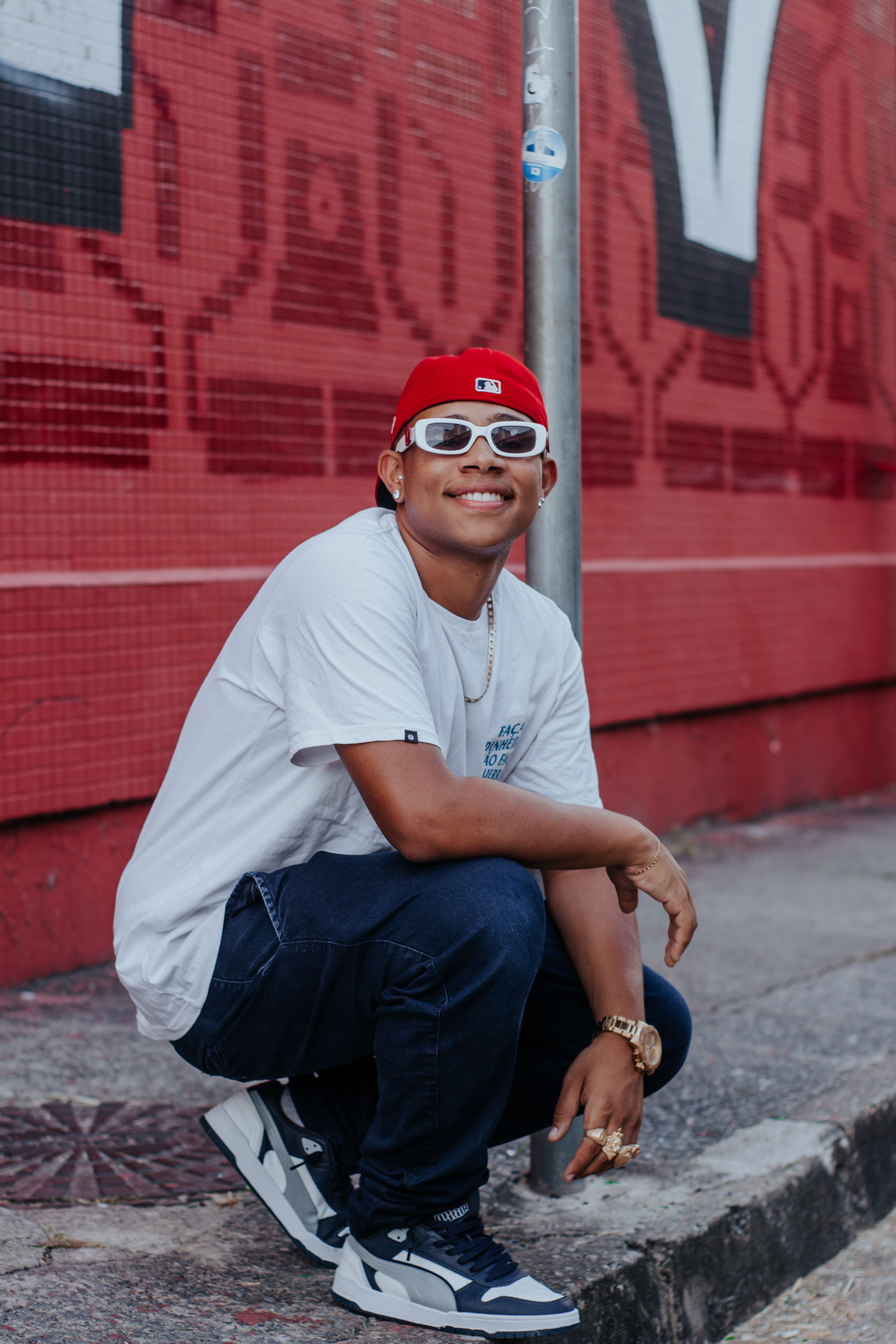 Stylish young man in urban streetwear crouching by a graffiti wall with a confident smile.