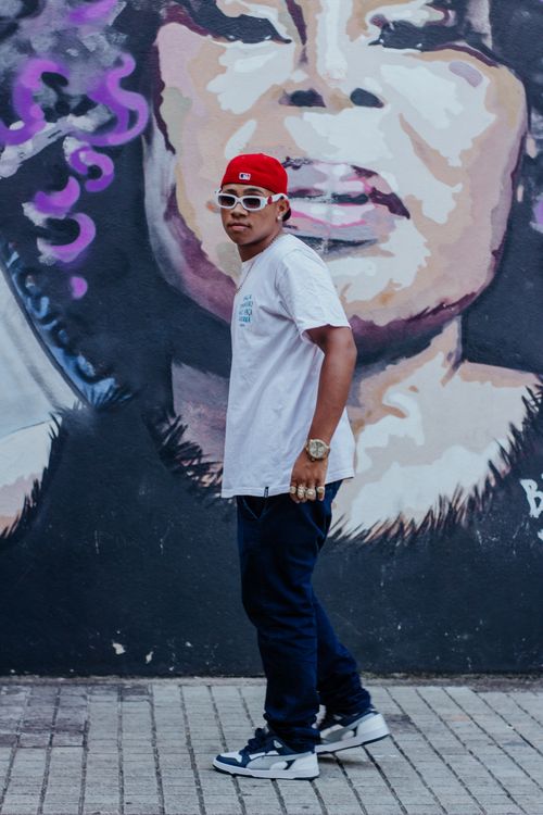 Free A young man with streetwear style stands against a colorful graffiti mural, wearing a cap and sunglasses. Stock Photo