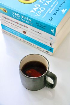 A cup of coffee beside a stack of colorful books on a white background.