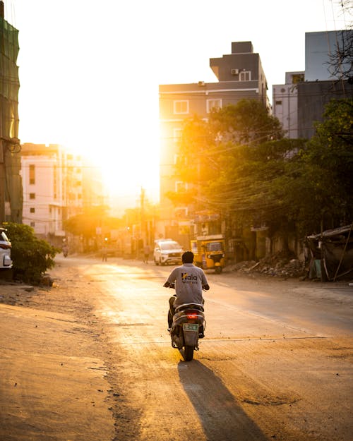 A man riding a motorcycle down a city street at sunset