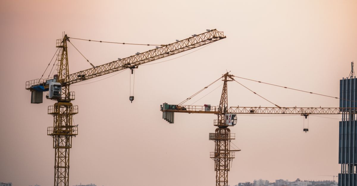 Skyline view of an urban construction site with prominent tower cranes at dusk.