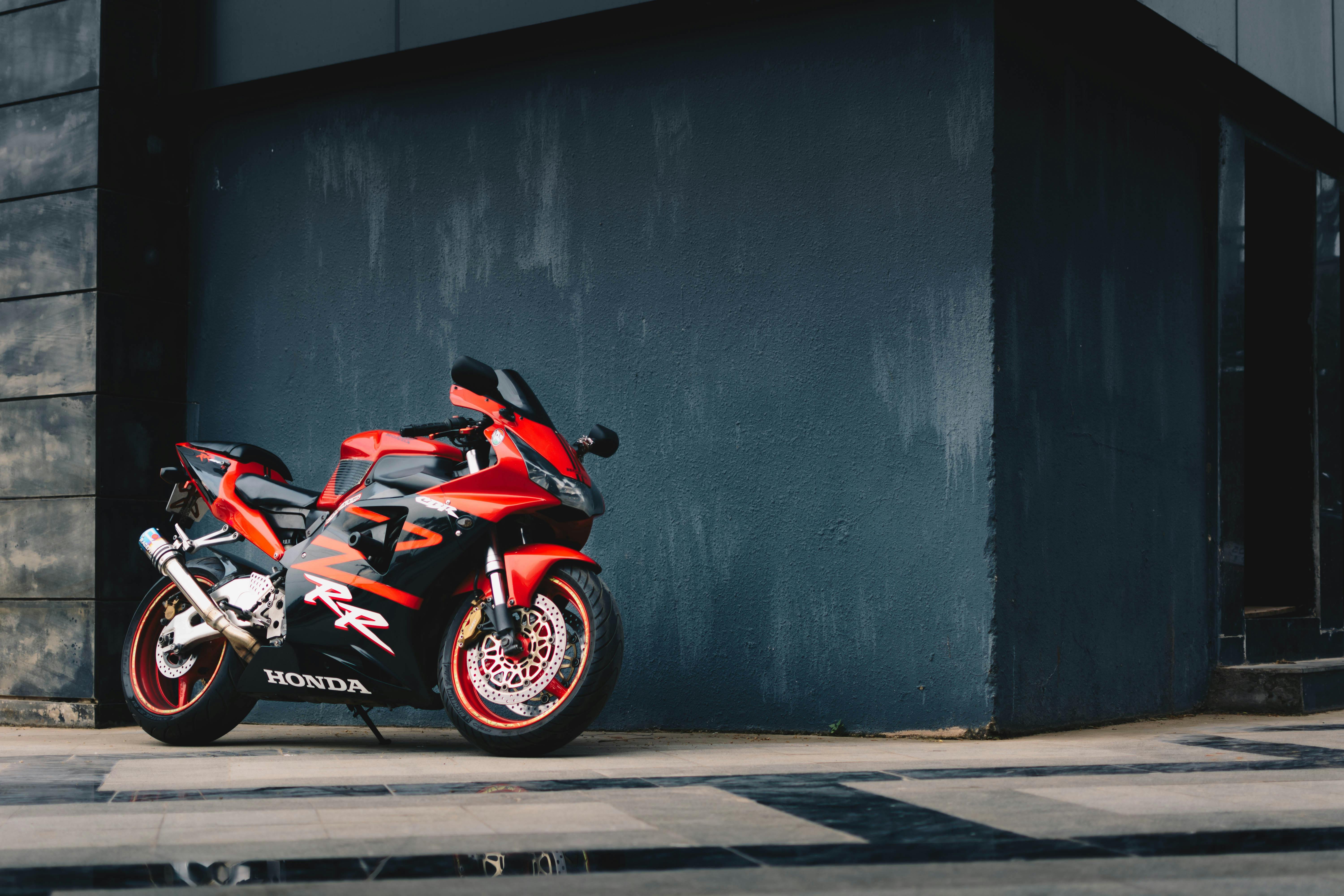 Photo of Red and Black Honda Sport Bike Parked Next to Black Wall · Free Stock Photo