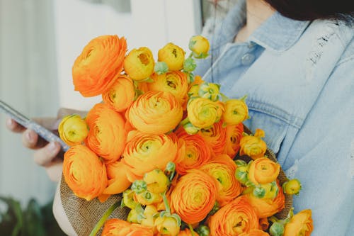 Crop female florist browsing smartphone while standing with bunch of yellow flowers